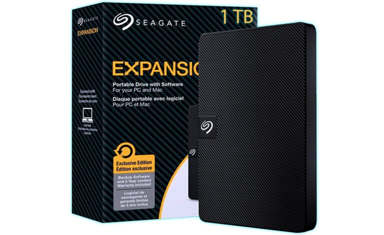 Seagate Expansion portable hard drive beside its black striped packaging, showing 1TB capacity and the Seagate logo on the box and drive surface.