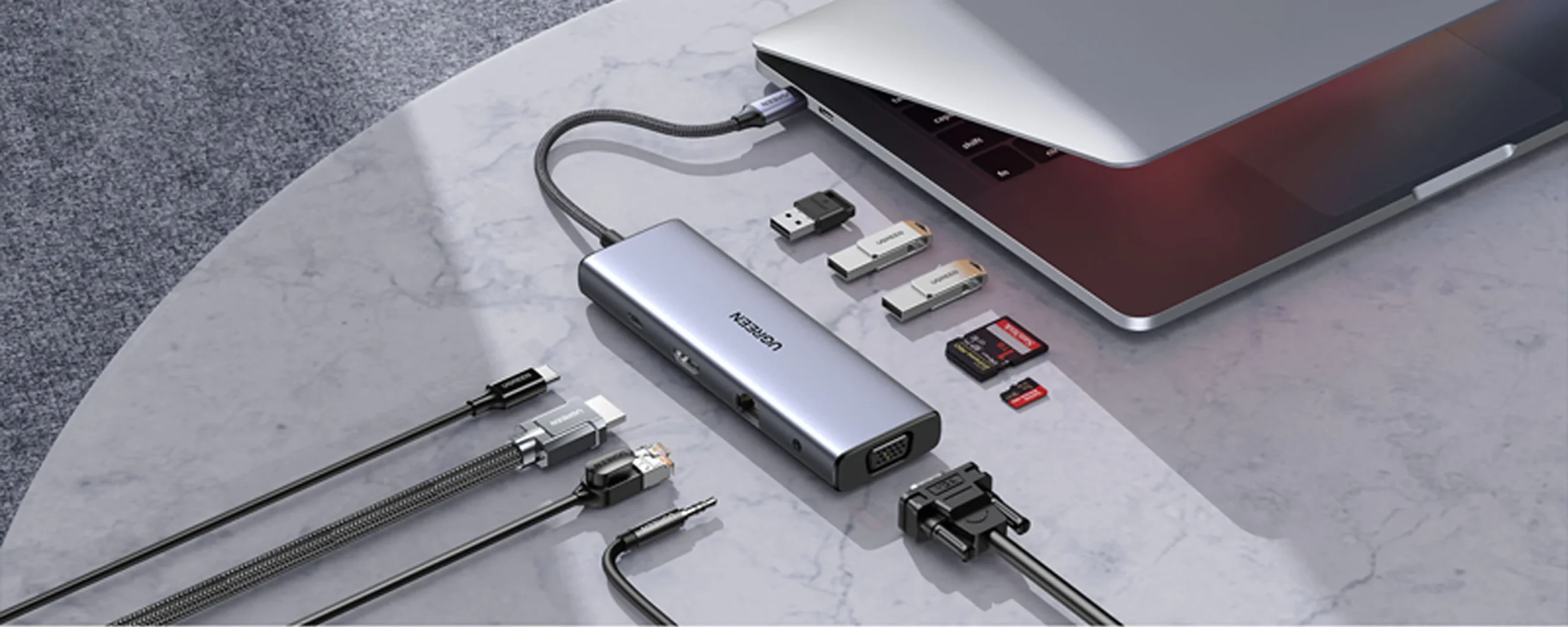 Silver USB-C hub connected to a laptop, surrounded by various adapters, memory cards and cables on a marble desk for expanded connectivity. | Ahoundjuè Technologies Silver USB-C hub connected to a laptop, surrounded by various adapters, memory cards and cables on a marble desk for expanded connectivity.