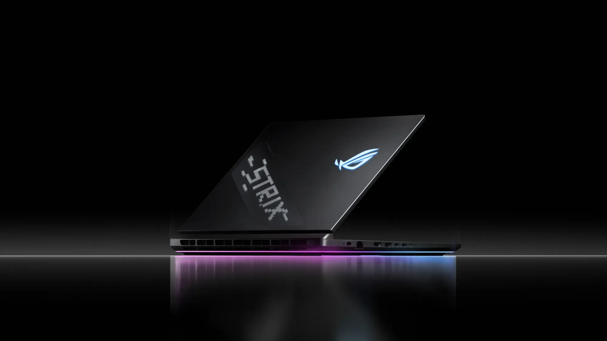Slim black gaming laptop tilted open on a dark reflective surface, with a blue logo and an RGB-lit base strip.