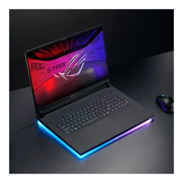 Gaming laptop with RGB-lit base and neon keyboard, open on a dark desk with a wireless mouse nearby (ROG Strix logo on screen).