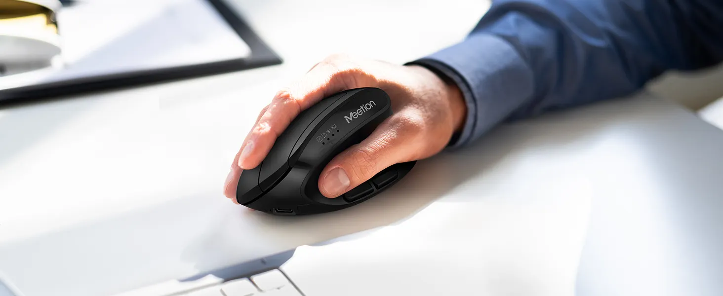 Close-up of a person’s hand gripping a black wireless computer mouse on a white desk, with a blue shirt sleeve visible.