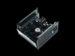 Internal view of a power supply unit showing capacitors, inductors, heat sinks, and circuit boards inside a metal chassis with a perforated side panel.