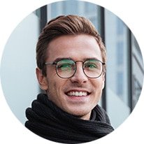 Portrait of a smiling man with brown hair and glasses wearing a black scarf, in an urban setting (circular crop).