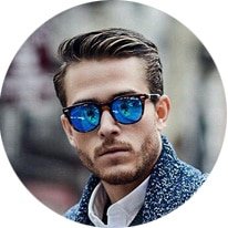 Man with short hair and beard wearing blue sunglasses and a patterned blue jacket, looking at the camera.