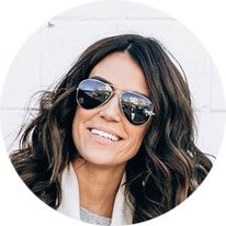 Smiling woman with long wavy hair wearing dark sunglasses, circular photo crop.