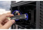 Hand inserting a Crucial T705 NVMe M.2 SSD into a desktop PC motherboard, blue-lit components visible inside the case. | Ahoundjuè Technologies Hand inserting a Crucial T705 NVMe M.2 SSD into a desktop PC motherboard, blue-lit components visible inside the case.