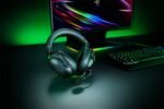 Over-ear gaming headset with attached mic on a dark desk, RGB-lit monitor and keyboard in the background
